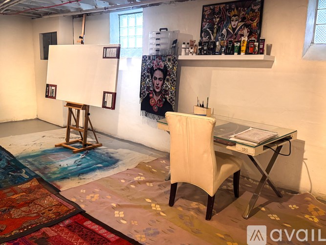 A room with a painting on a canvas on a stand, a chair, a table, and a painting on the wall.
