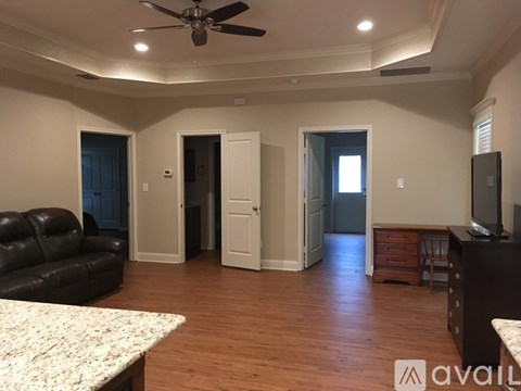 A living room with a black leather couch and a ceiling fan.