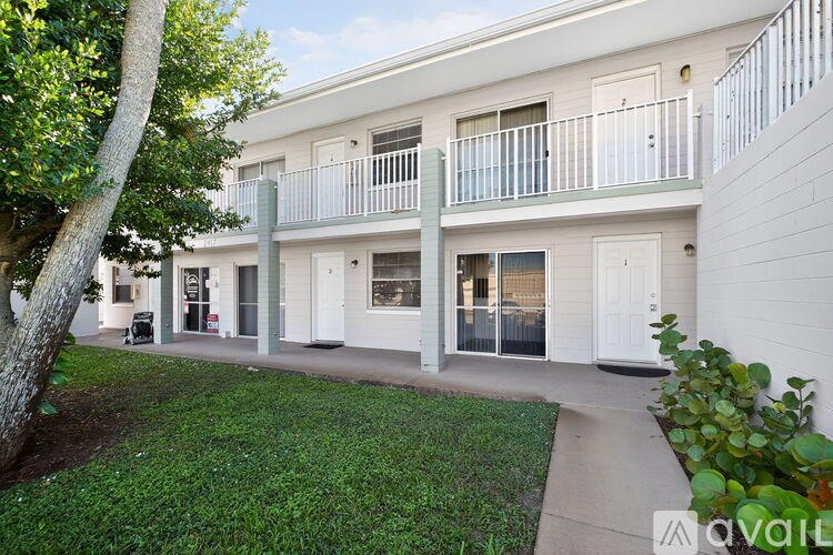 A building with white balconies and doors is surrounded by greenery.