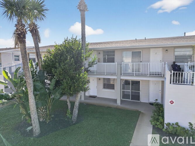 A balcony with a railing overlooks a small garden with a palm tree.