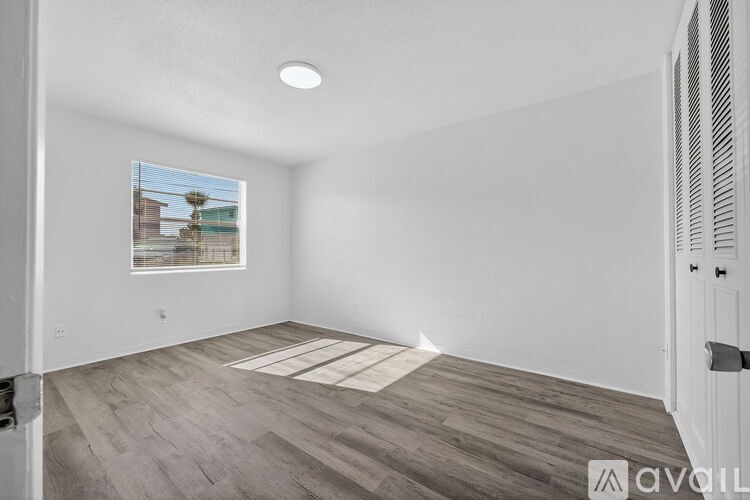 A room with a wooden floor and a window showing a building outside.