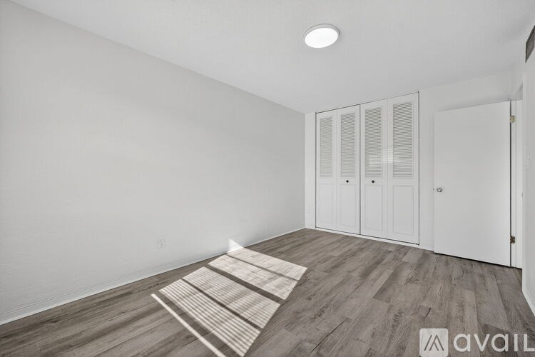 A room with a wooden floor and white walls, with a rug on the floor and a door on the right side.