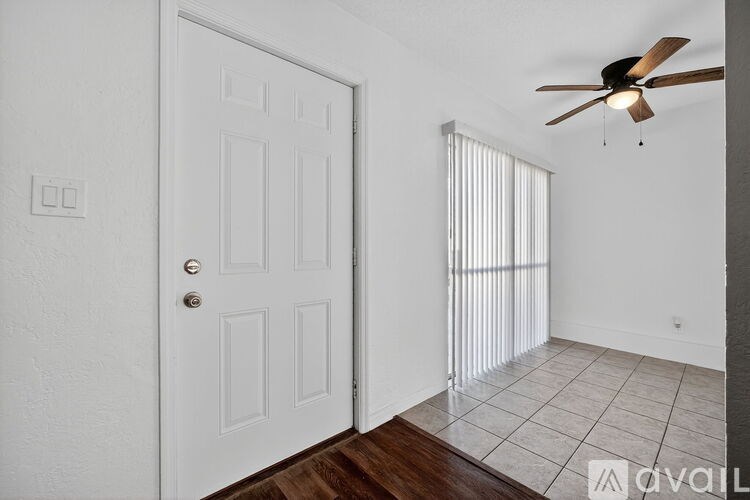 A room with a white door, a ceiling fan, and a window with blinds.