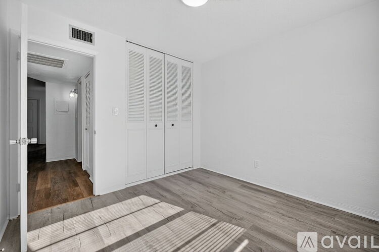 A room with a wooden floor and white walls, featuring a set of white closet doors.