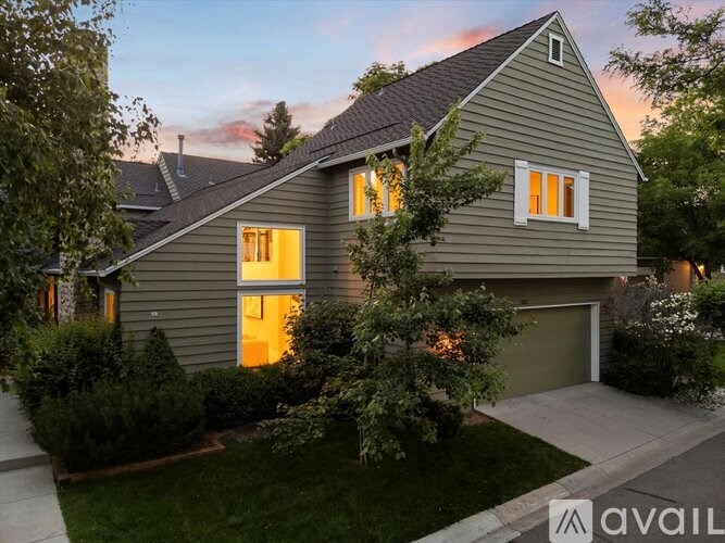 A house with a grey exterior and a brown roof is shown with the sun setting in the background.