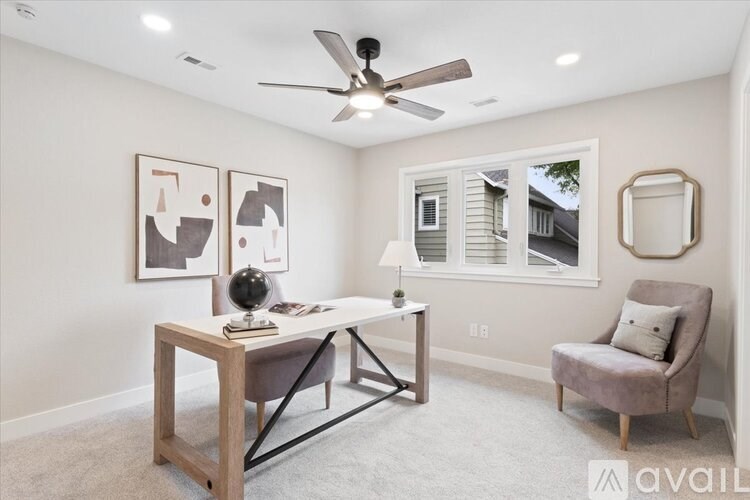 A room with a ceiling fan, a table with a chair, and two framed pictures on the wall.