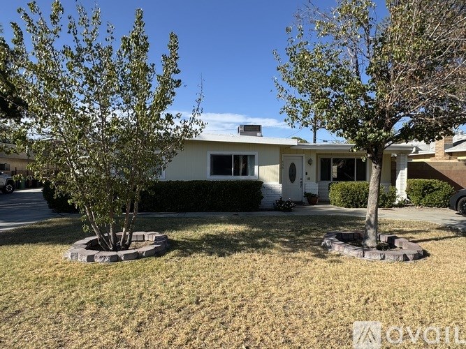 A house with a white exterior and a grey roof is surrounded by two trees.