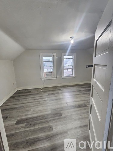 A room with wooden flooring and two windows.