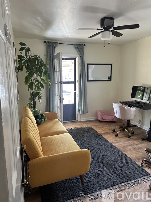 A yellow chair is in the corner of a room with a ceiling fan.