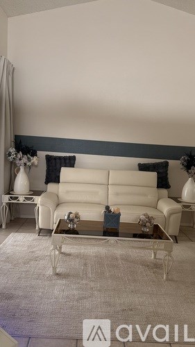 A white sofa with a grey cushion is in the middle of a room with a glass coffee table in front of it.