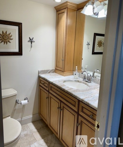 A bathroom with a toilet, sink, and cabinets.
