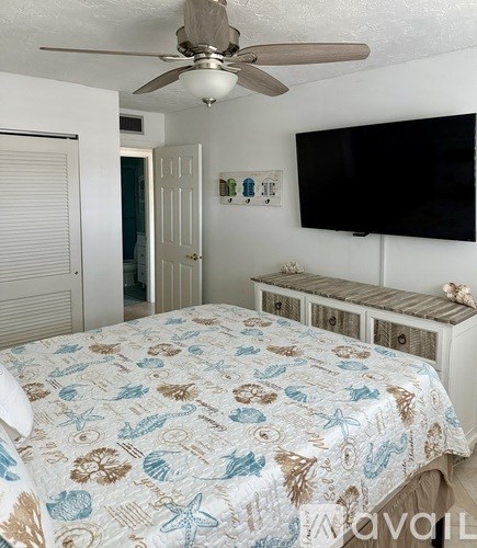 A bedroom with a bed, a ceiling fan, and a television mounted on the wall.