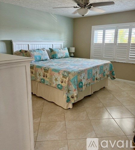 A bedroom with a bed covered in a patterned bedspread and a ceiling fan.