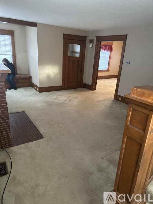 A man is sitting on a bench in a room with a brown door and a window.