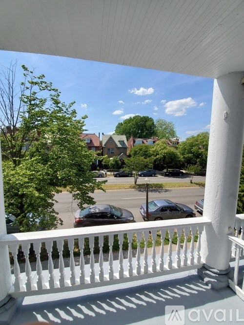 A balcony with a white railing overlooks a street with cars and houses.