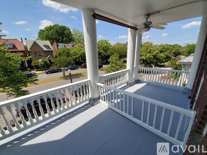 A balcony with white railings and a view of a street with cars and houses.