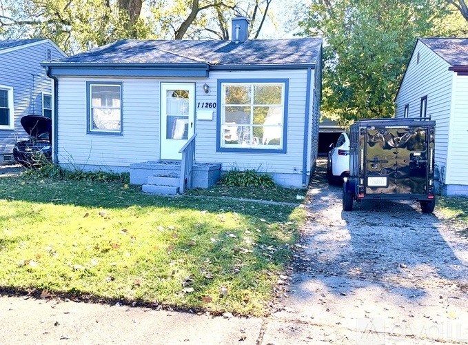 A small blue house with a white door and windows is in front of a white house.