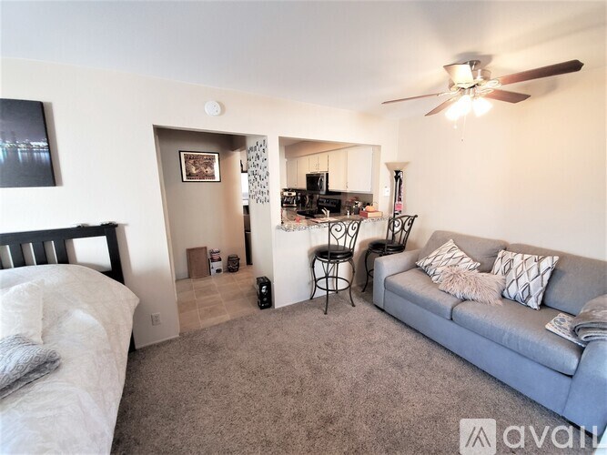 A living room with a grey couch and a bed with white sheets.