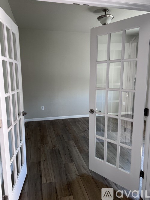A white door with glass panels is open to a room with wood flooring.