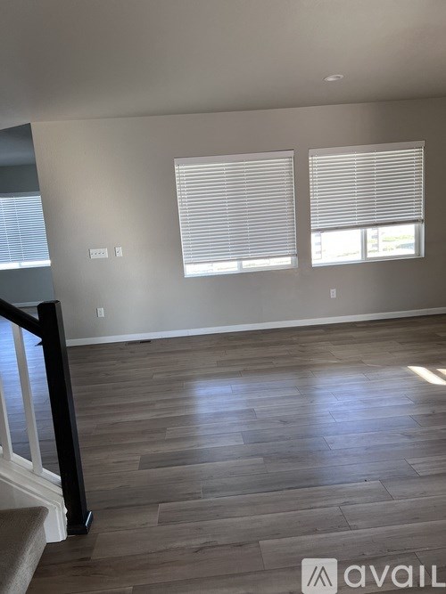 A room with wooden flooring and two windows with blinds.