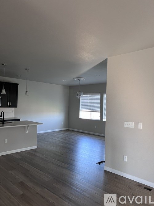 A spacious room with wooden flooring and a kitchen area with white cabinets.