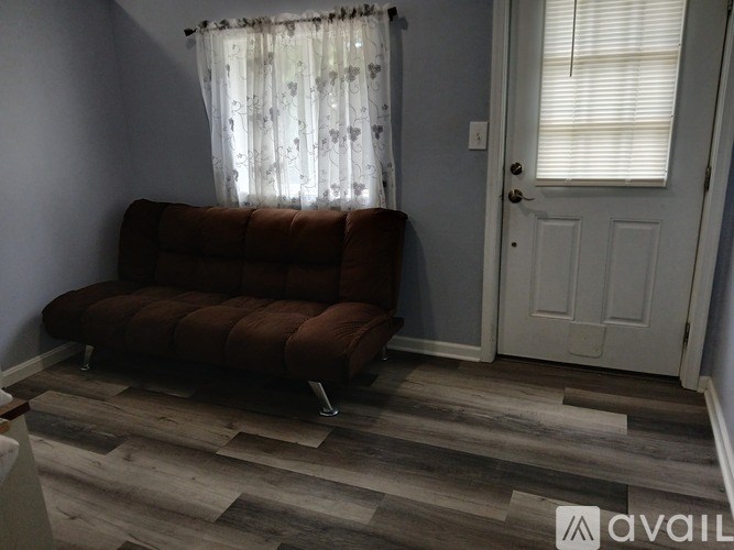 A brown sofa is in the corner of a room with a window and a door.