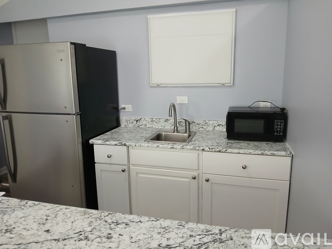 A kitchen with a black fridge, white cabinets, and a granite countertop.