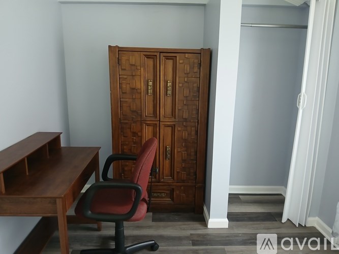 A brown wooden cabinet with a door is in a room with a red chair and a wooden desk.