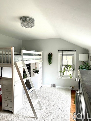 A white bunk bed with a ladder is in a room with a window and plants.