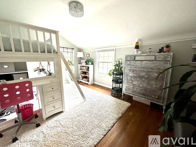 A room with a white desk and a white chair with a red cushion.