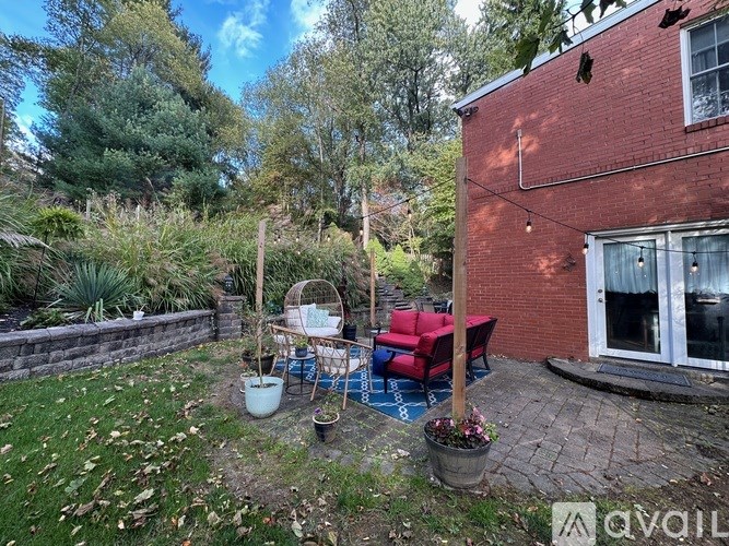 A backyard with a red couch, a wicker chair, and a white pot.