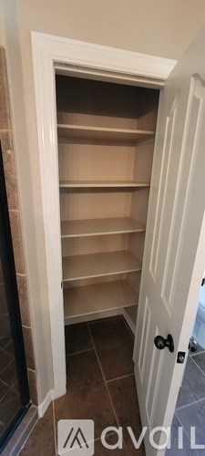 A white door with a black handle is open to a room with empty shelves.