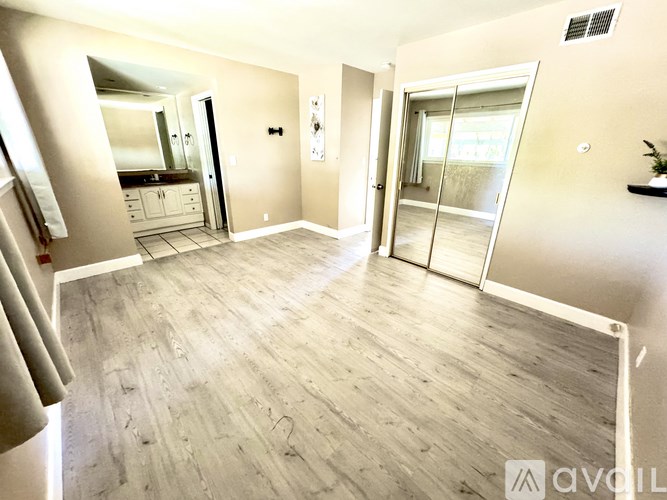 A spacious room with wooden flooring and a sliding glass door leading to a balcony.