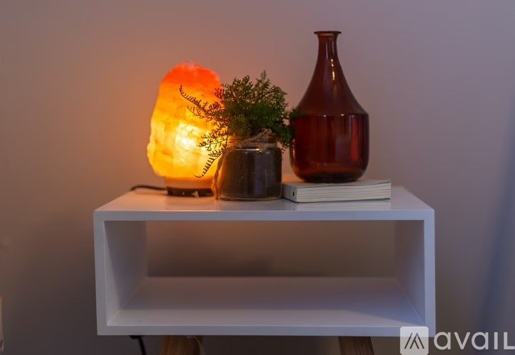 A white shelf with a glowing orange lamp, a green plant, and a red vase on it.