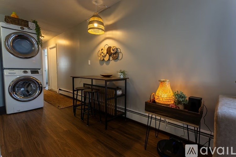 A room with a washing machine on the left and a table with a lamp on the right.