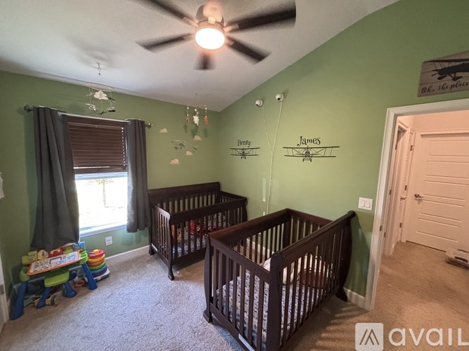 A baby room with two cribs and a ceiling fan.