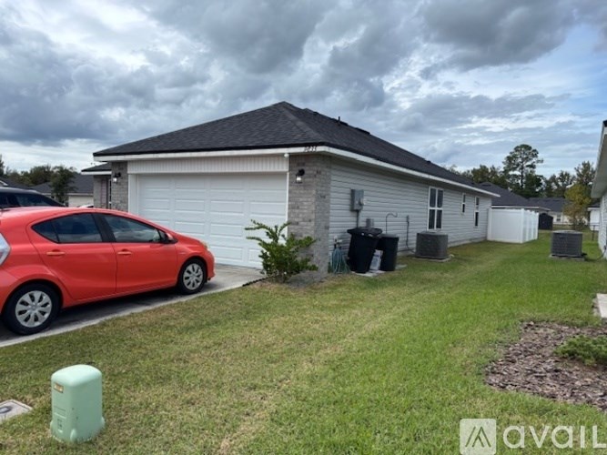 A red car is parked in front of a grey house.