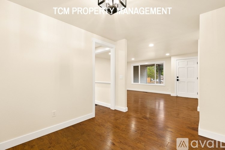 A room with wooden flooring and white walls, with a doorway leading to another room.