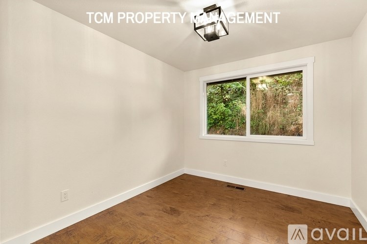 A room with wooden flooring and a window showing greenery outside.