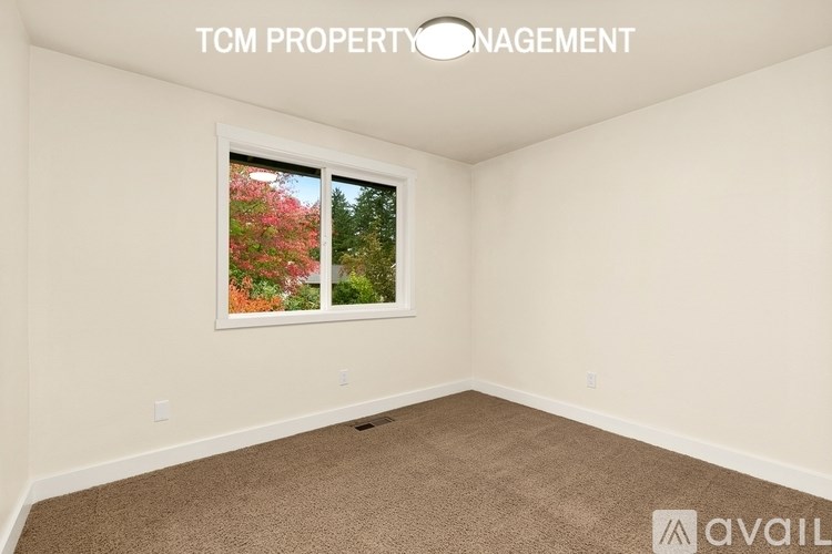 A room with a window showing a view of trees and flowers.