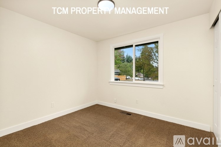 A room with a carpeted floor and a window showing trees and a building outside.