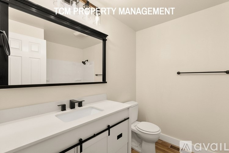 A bathroom with a white sink and toilet, a mirror, and a black barrier.