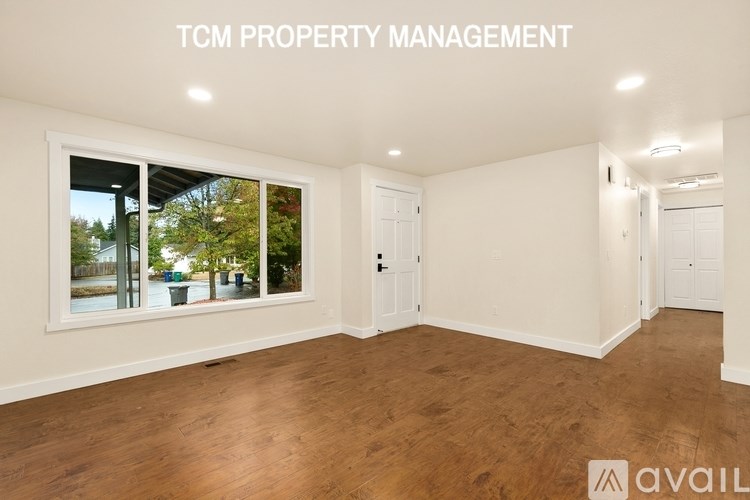 A room with wooden flooring and a large window showing an outdoor scene.