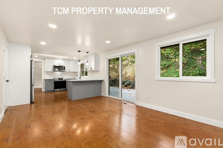A spacious kitchen and living room with wood flooring and a view of trees outside the window.