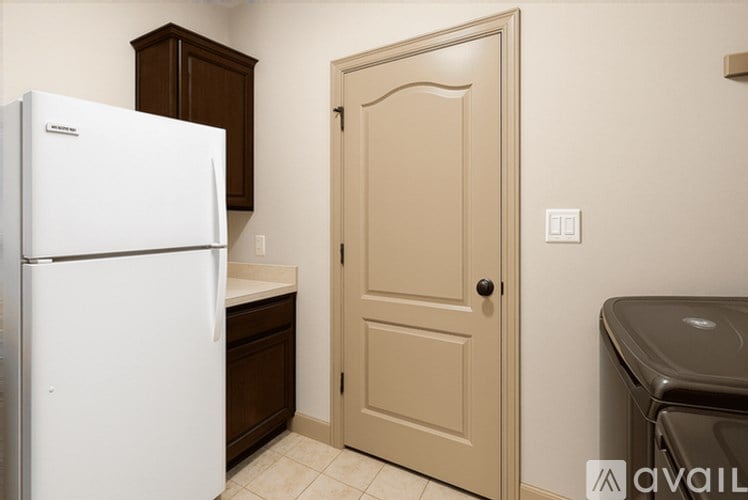 A white refrigerator in a kitchen with a brown cabinet and a beige door.