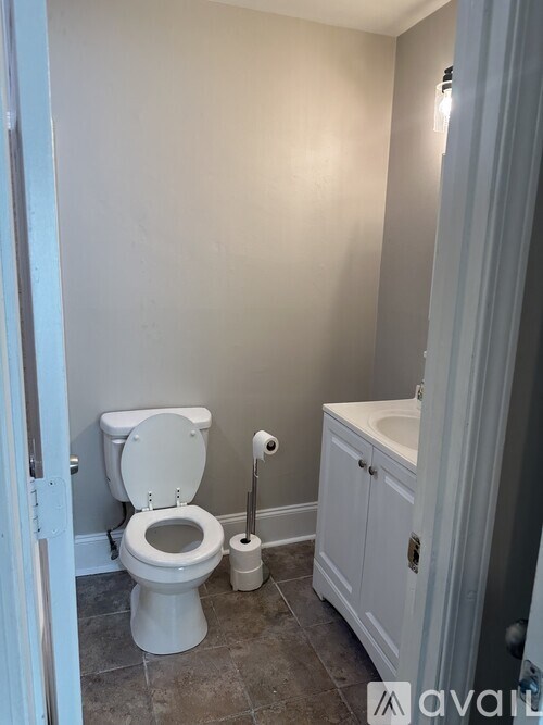 A white toilet with a roll of toilet paper and a white sink with a cabinet underneath it.
