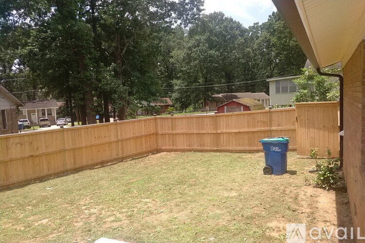 A backyard with a wooden fence and a blue trash bin.
