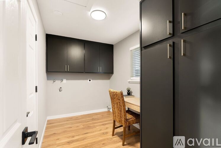 A black fridge sits next to a desk with a chair in a room.