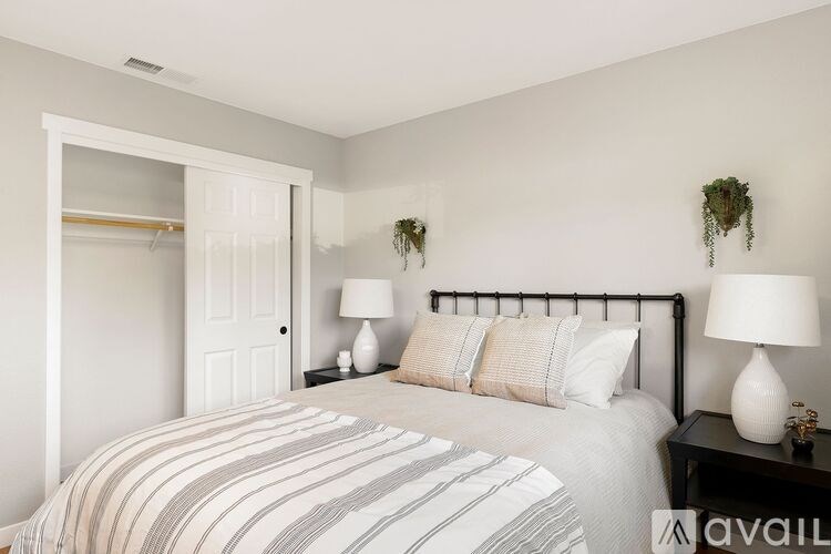 A bedroom with a bed, two lamps, and a plant on the wall.