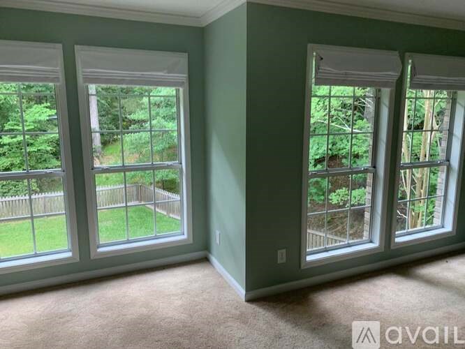 A room with three windows overlooking a green backyard.